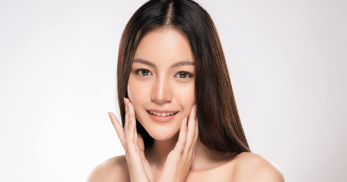 A young woman with glowing, smooth skin gently touches her face and smiles, representing the rejuvenating effects of PRP Treatments in Las Vegas, NV.